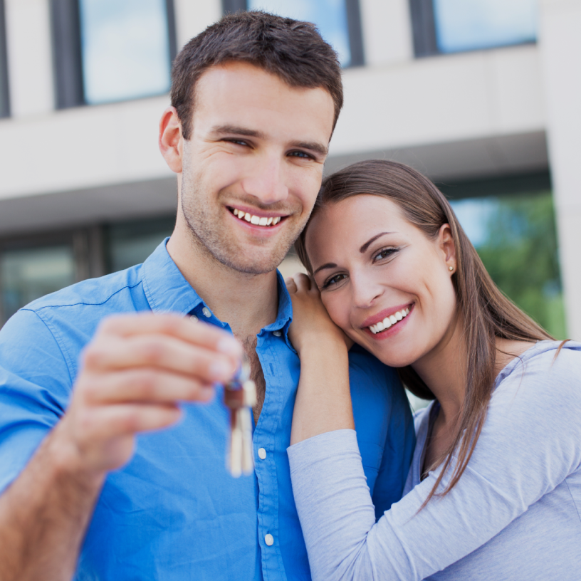 Excited couple holding the keys to their new home, celebrating their milestone of becoming homeowners.