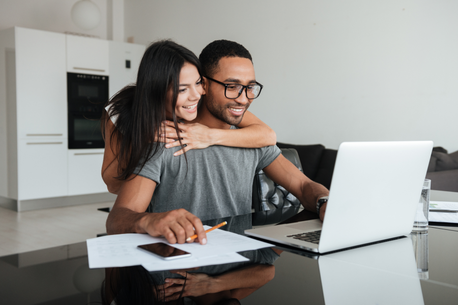 Happy couple sitting together, using a laptop to manage finances or make decisions in their cozy living room.