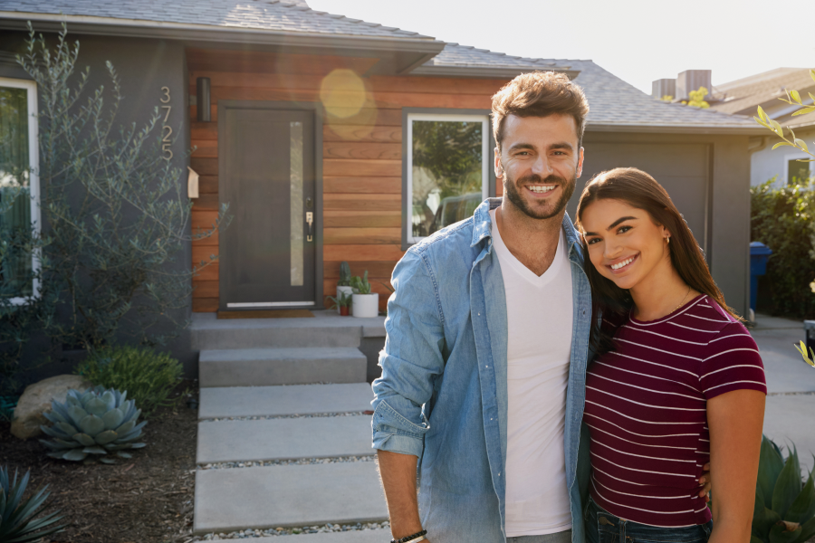 Smiling young couple standing together in front of their new home, enjoying their achievement of homeownership.